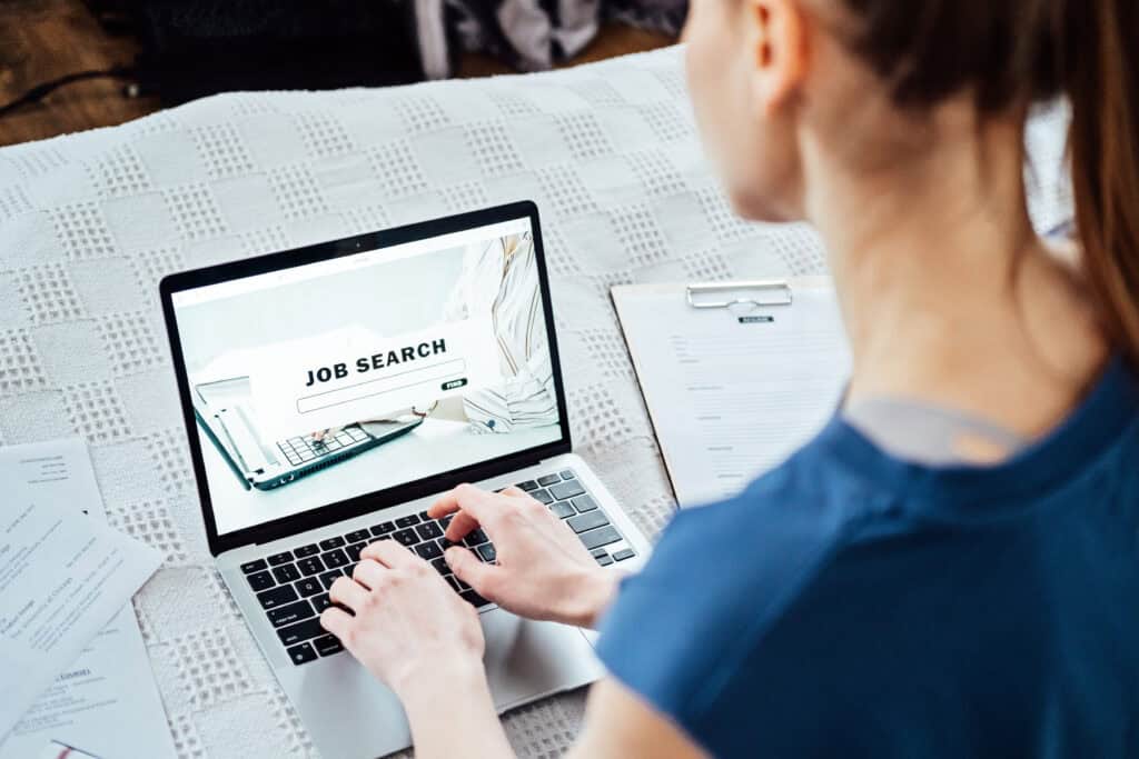 Person using a laptop for a job search in Oklahoma with a resume nearby.