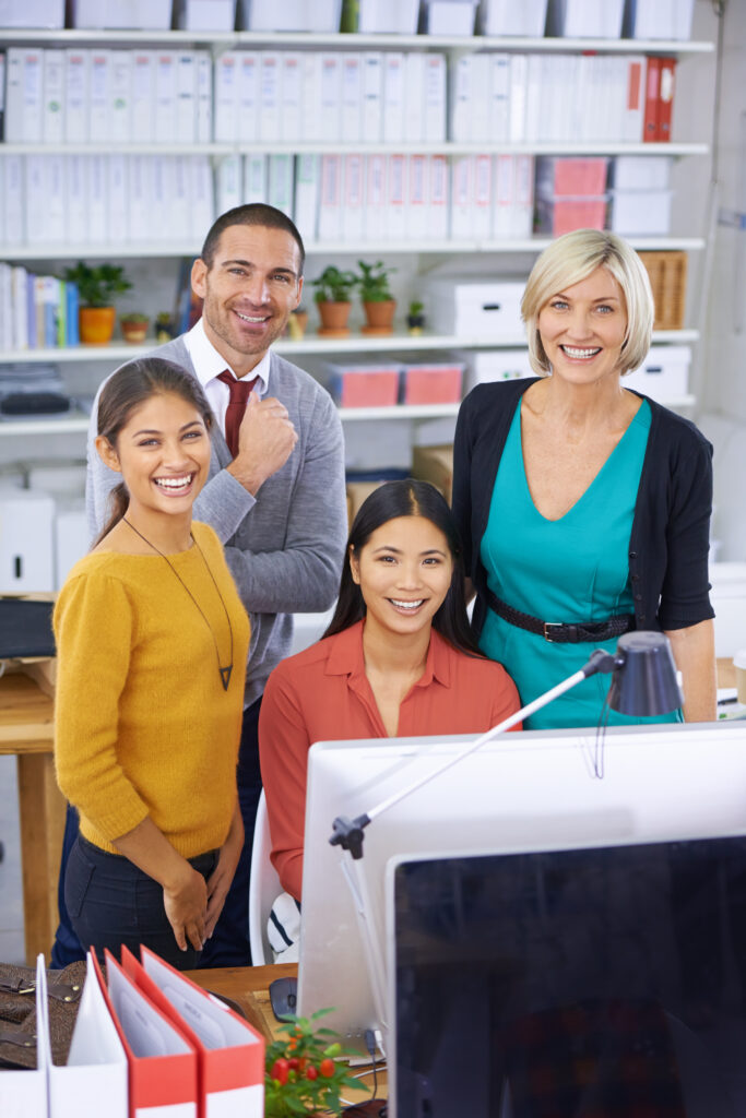Smiling office team gathered around a computer with support from an Oklahoma staffing agency providing office staffing and recruiting services